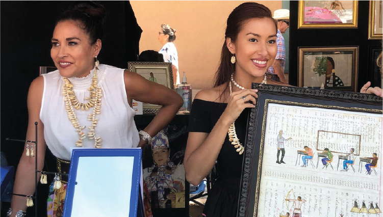 Two Native American women artists at an art show, one is holding up an example of ledger art. Image is for the documentary, The Art of Home: A Wind River Story