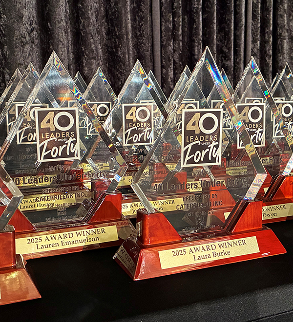 A group of 40 Leaders Under Forty Awards sitting on a table in front of black drapes
