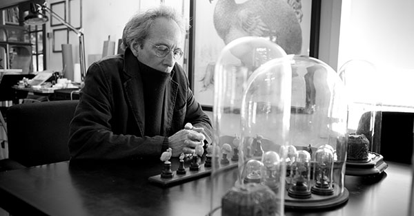 A person sits at a table with glass domes and figurines, in a black and white photo.