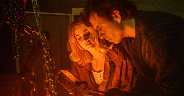 Two people examining an object with chains, illuminated by a warm light, in a dimly lit room.