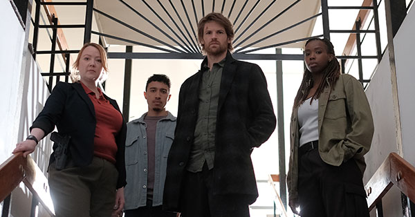 Four people standing on stairs, looking forward, with geometric railing design in the background.