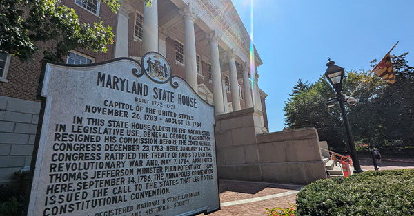 Historic marker in front of the Maryland State House with columns and trees in the background.