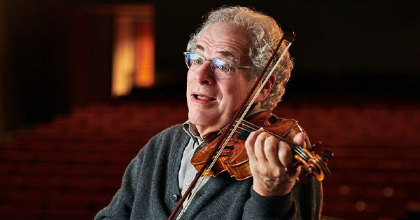 Person playing violin with a thoughtful expression in a dimly lit room.