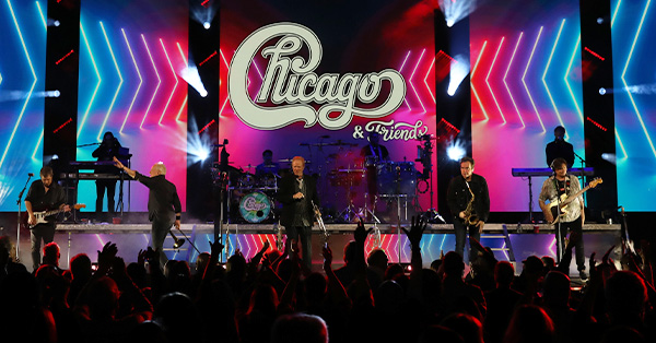 Performers on stage with the Chicago, a Tribute Logo in the background.