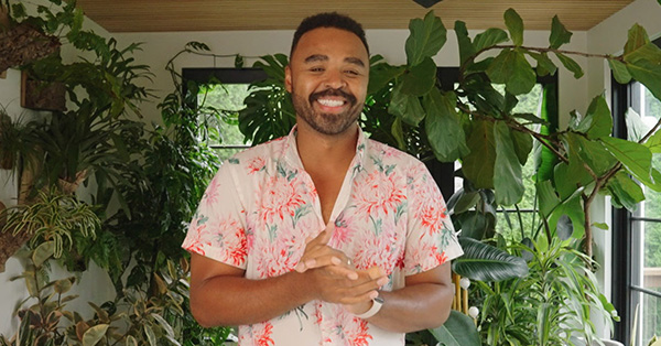 Hilton Carter smiling while standing in front of large house plants.
