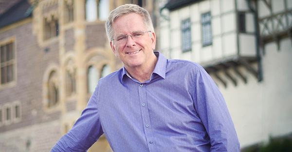 Rick Steves posing for a photo in front of European looking buildings.