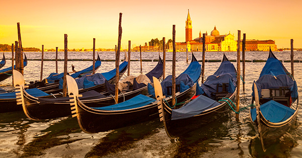 A serene sunrise over the Venetian Lagoon in Venice, Italy, featuring traditional gondolas moored in the foreground. 