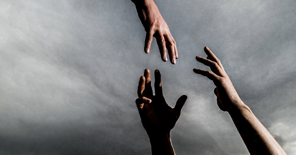 Three hands reach for each other with a gray sky in the background,