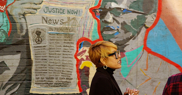 Akemi Kochiyama stands in front of the From Harlem with Love mural of her grandmother Yuri Kochiyama and Black Panther leader Malcolm X