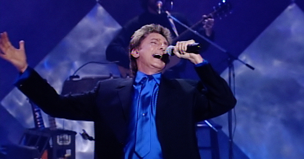 Beloved singer/songwriter Barry Manilow sings fan favorites on stage in front of musicians.