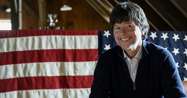 Ken Burns Sitting in front of the United States Flag.