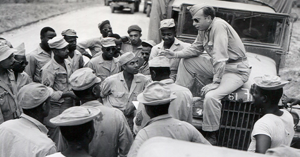 WWII Black soldiers being briefed by white battalion leader sitting on truck while standing on road