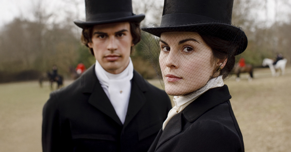  Theo James as Mr. Pamuk and Michelle Dockery as Lady Mary standing outside in front of a fox hunt.