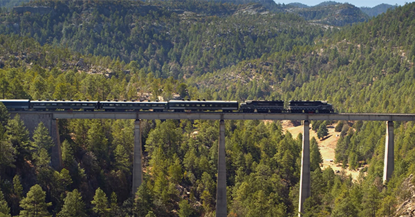 Train traveling over a bridge spanning a deep gorge in the mountains.