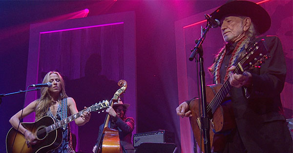 Sheryl Crow and Willie Nelson perform on stage.