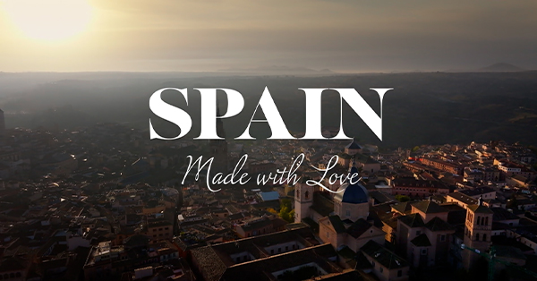 Promotional image for Spain Made with Love featuring an aerial view of a historic Spanish city at sunrise. The program title appears prominently over the skyline.